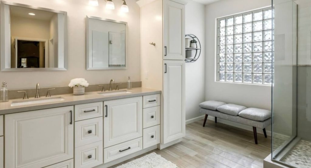 Remodeled bathroom with a white double vanity, glass-block window and a bench by the shower