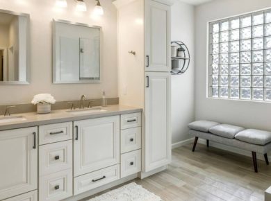 Remodeled bathroom with a white double vanity, glass-block window and a bench by the shower