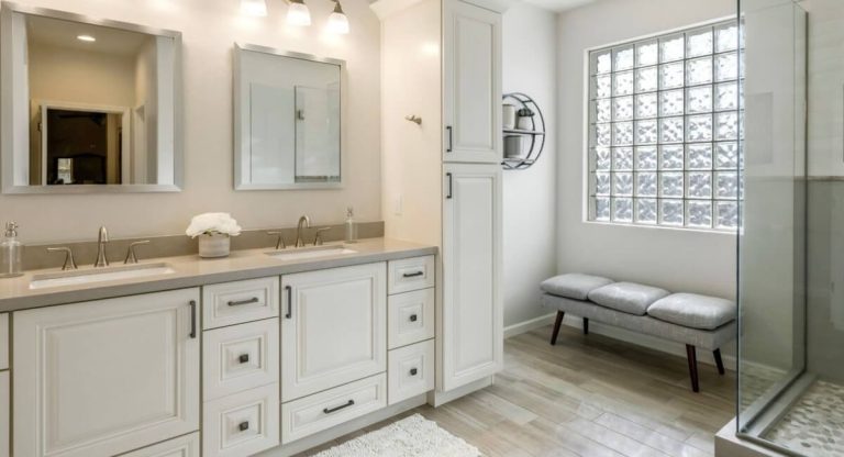 Remodeled bathroom with a white double vanity, glass-block window and a bench by the shower