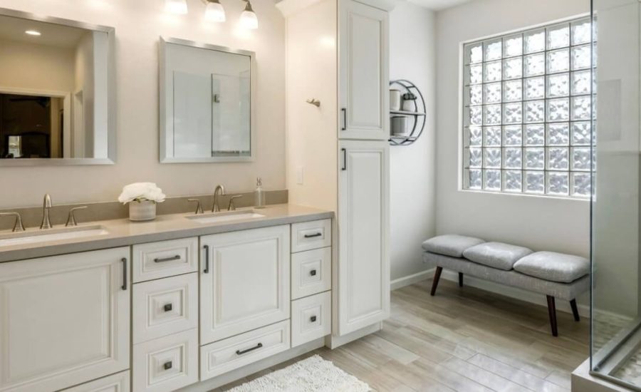 Remodeled bathroom with a white double vanity, glass-block window and a bench by the shower