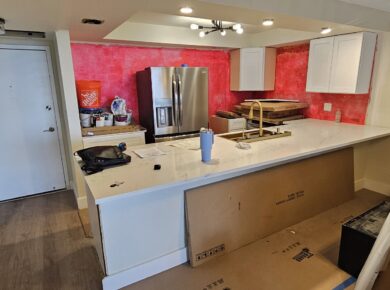 Condo kitchen mid-remodel: white shaker cabinets and quartz island installed, walls still unpainted