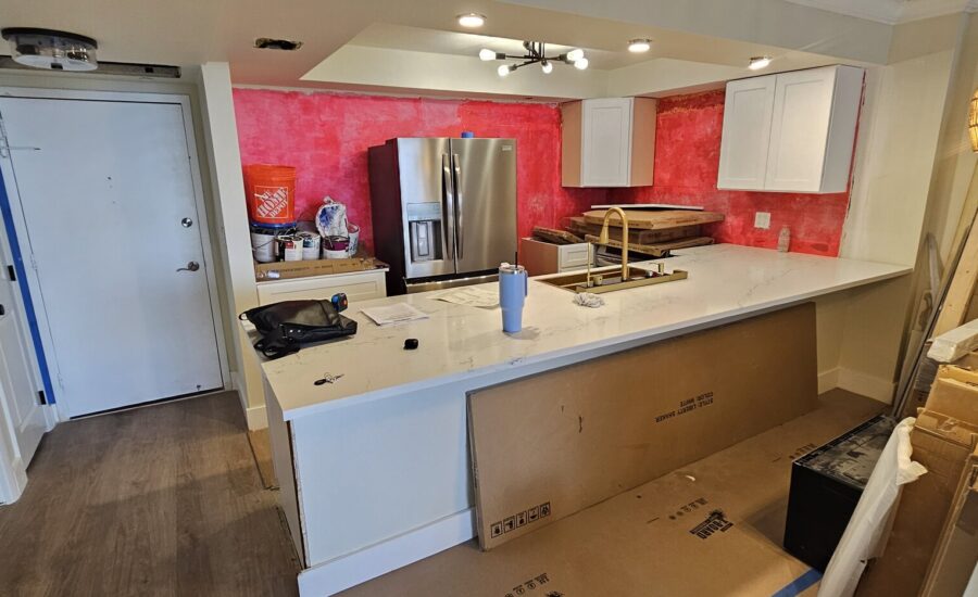 Condo kitchen mid-remodel: white shaker cabinets and quartz island installed, walls still unpainted