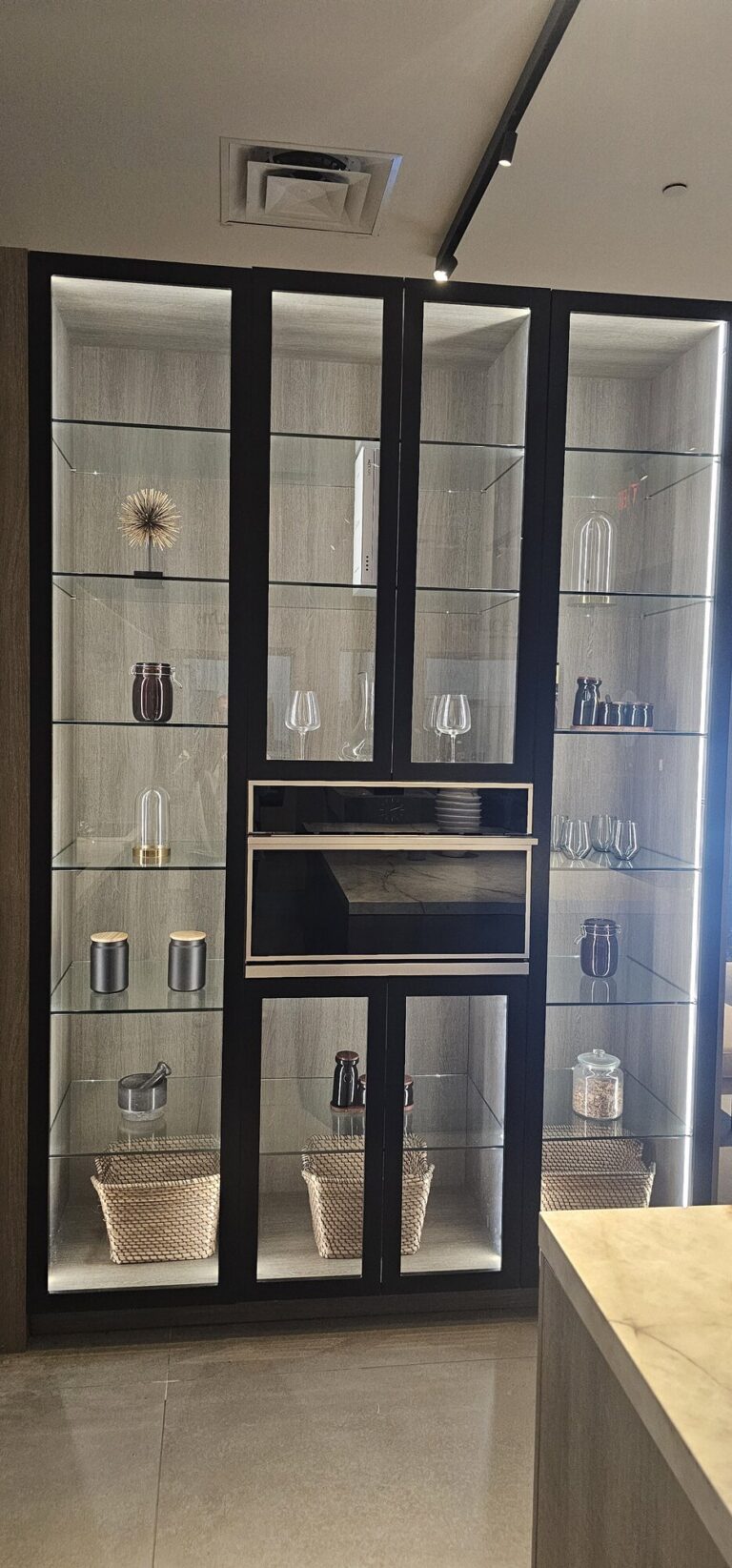 Showroom display of tall black-framed glass-front cabinets with lit glass shelves