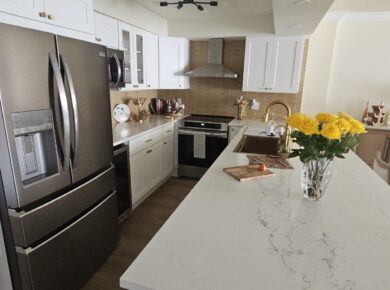 White shaker kitchen with a marble-look quartz island, gold faucet and stainless appliances