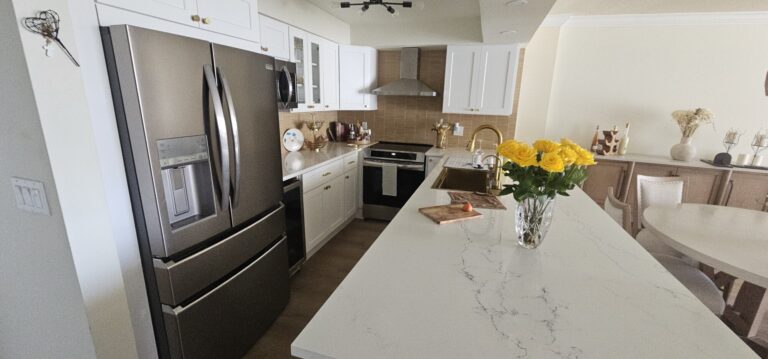 White shaker kitchen with a marble-look quartz island, gold faucet and stainless appliances