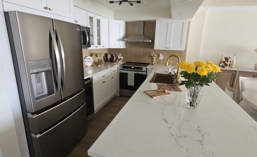 White shaker kitchen with a marble-look quartz island, gold faucet and stainless appliances