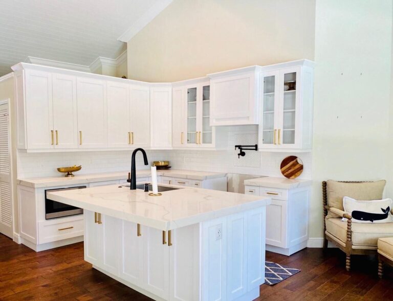White shaker kitchen with brass pulls and glass-front upper cabinets under a vaulted beadboard ceiling, a quartz island with a black faucet, a pot filler and a microwave drawer