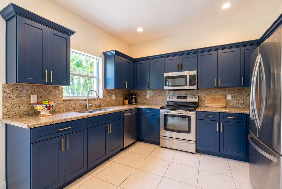 A 1990s kitchen refaced with navy shaker doors and brass bar pulls; the granite counters, sink and appliances are unchanged