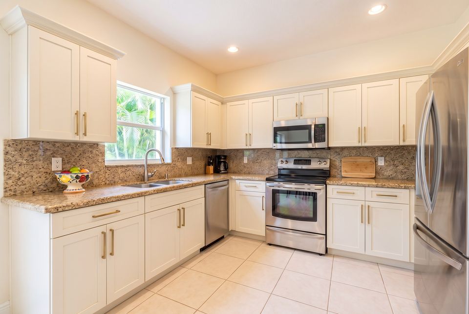 After: the same kitchen with warm white shaker doors and brushed brass bar pulls; counters, sink, appliances and floor unchanged