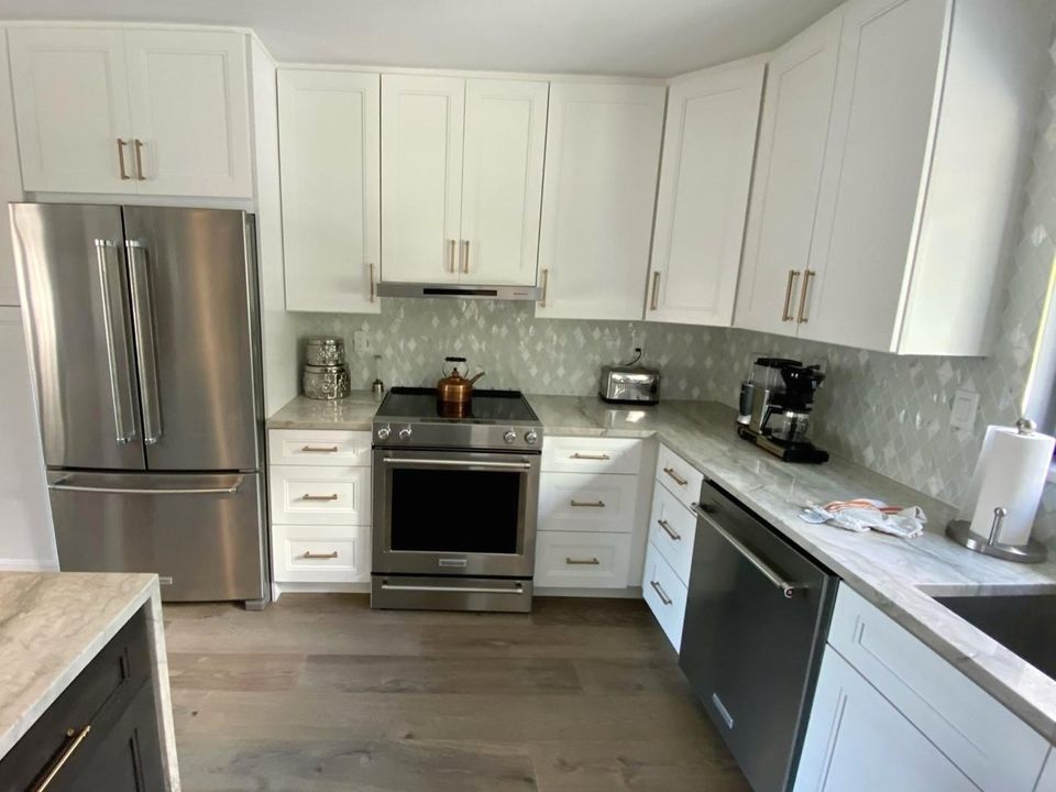 Before: an L-shaped kitchen with white shaker cabinets, gold pulls, stone counters and a grey mosaic backsplash